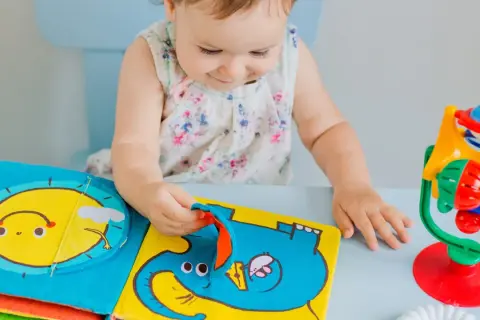 Dziecko bawi się kolorową książeczką sensoryczną z motywem słonia i słońca.