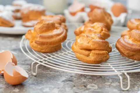 Färska petit choux på ett galler, med äggskal i förgrunden. Perfekt för en fika!