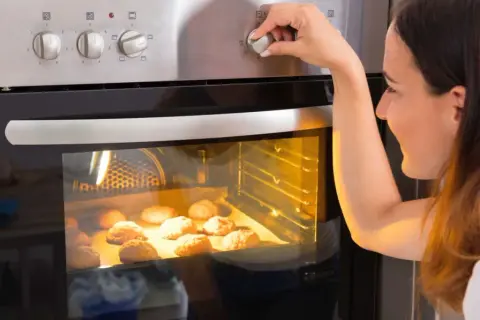 Kobieta ustawia temperaturę piekarnika, zastanawiając się, ile prądu zużywa piekarnik podczas pieczenia ciasteczek.