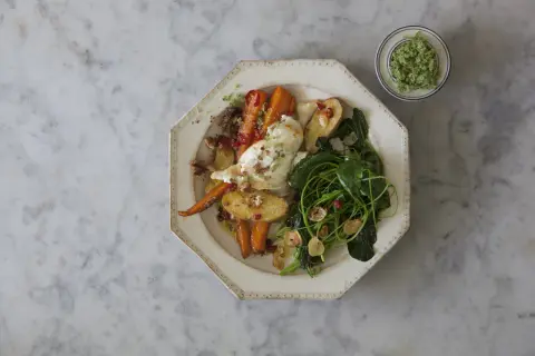 Ugnsrostade rotfrukter med fetaost, serverade med gröna blad och en grön topping.