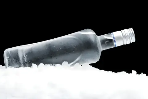 Szklana butelka z wódką leży w lodzie, tworząc wrażenie, czy wodka sie zamrozi.