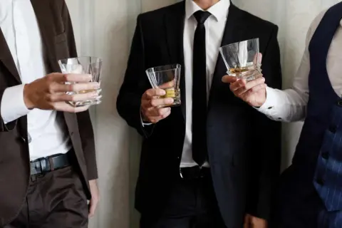 Uomini eleganti con bicchieri di whisky, perfetti per un dress code cocktail.