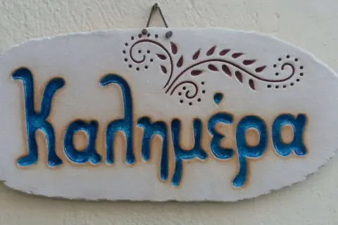 Ceramiczna tabliczka z napisem "Καλημέρα" (Dzień dobry) po grecku, ozdobiona roślinnym motywem.