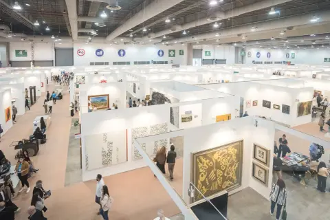 A bustling scene at the Mexico City Art Fair, with visitors exploring numerous white-walled booths showcasing diverse artworks.