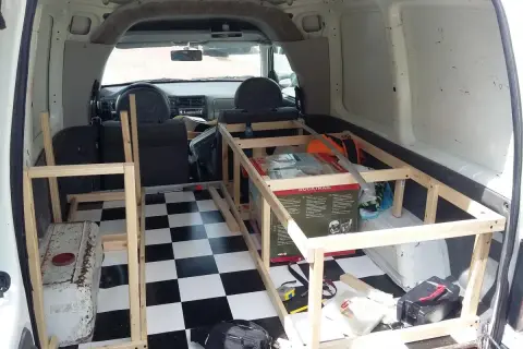 Wnętrze vana przerabiane na minicamper. Drewniana konstrukcja łóżka, szachownica na podłodze, skrzynka narzędziowa.