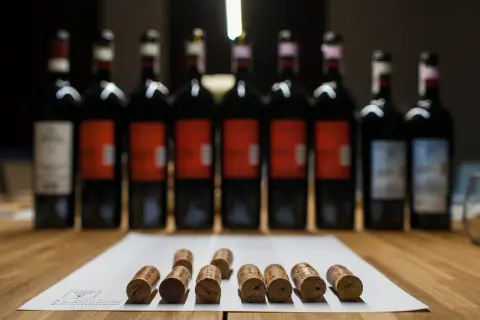 Rząd butelek wina, w tym wino brunello, i korki na papierze.