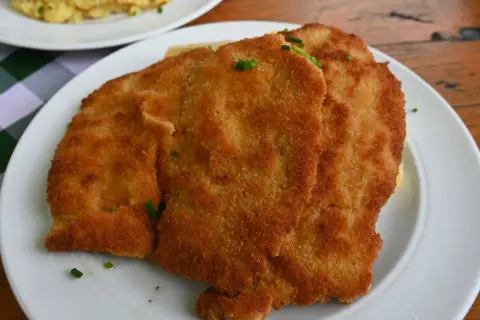 Zwei goldbraune Schnitzel auf einem Teller, garniert mit Schnittlauch. Ein Klassiker der Berliner Küche, der Appetit macht.