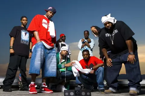 Grupa raperów z Wu-Tang Clan pozuje do zdjęcia na tle nieba.