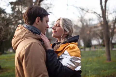 Para, która patrzy sobie w oczy w parku. Ona delikatnie dotyka jego policzka. Zastanawiasz się, czy napisać do faceta, który przestał się odzywać?