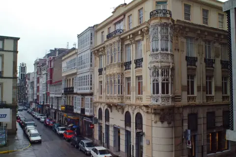 Edificios con balcones acristalados y una torre ornamental en una calle de Ferrol. Merece la pena visitar Ferrol por su arquitectura única.