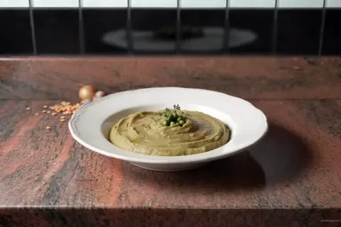 Une assiette de purée de pois cassés, garnie de petits pois et d'herbes, sur un plan de travail en granit.