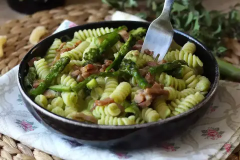 En härlig pastarätt med sparris och bacon, perfekt för ett snabbt sparris recept. En gaffel sticker upp ur den krämiga pastan.
