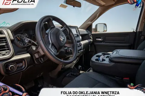 Wnętrze samochodu po oklejaniu deski rozdzielczej folią. Widok na kierownicę, konsolę środkową i siedzenie.