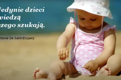 Małe dziecko w różowym stroju kąpielowym i kapeluszu siedzi na plaży. Cytat: "Jedynie dzieci wiedzą czego szukają.