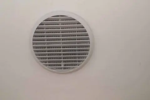 Foro ventilazione cucina entra freddo. La griglia bianca circolare è montata su una parete chiara.