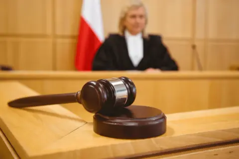 Młotek sędziowski na stole w sali sądowej, obok polska flaga. Sędzia w todze w tle. Ile apelacji jest oddalanych?
