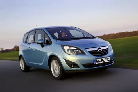 Niebieski Opel Meriva 1.4 benzyna w ruchu, z kierowcą za kierownicą, na tle zielonych pól i drzew.