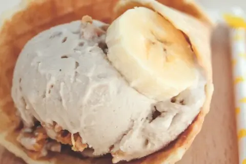 Delicioso helado de crema de cacahuete en un cono de gofre, coronado con rodajas de plátano.