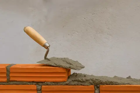 Cazzuola con malta a base di calce pronta per posare un mattone su una parete in costruzione.