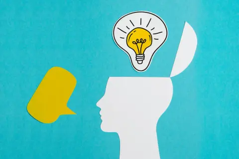 Psychologia obrazki: biała głowa z otwartą czaszką, w której świeci żarówka pomysłu, obok żółty dymek.