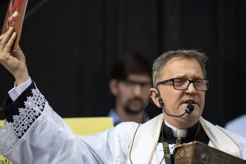 Ksiądz Michał Woźnicki w białej albie z koronkowymi mankietami podnosi obrazek, przemawiając do wiernych.