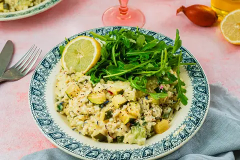 Un crémeux risotto courgette, garni de roquette fraîche et d'une tranche de citron, sur une assiette ornée.