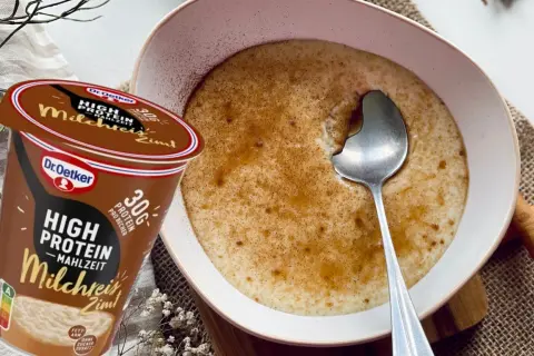 Schüssel mit Milchreis mit Zimt, daneben ein Becher "High Protein Milchreis Zimt" von Dr. Oetker.