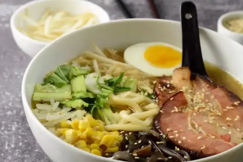 Jak zrobić ramen? Miska pełna aromatycznego bulionu z makaronem, plastrem boczku, jajkiem na pół, pak choi, kukurydzą i grzybami mun.