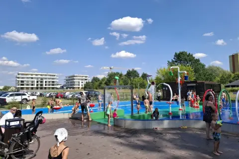 Dzieci bawią się na wodnym placu zabaw przy zalewie Borki. Woda tryska z kolorowych elementów, tworząc radosną atmosferę.
