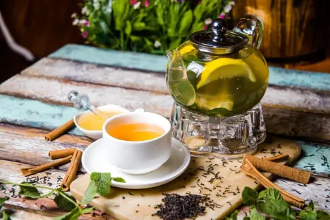 Aromatyczna zielona herbata parzenie na uspokojenie z cytryną i miodem. Na stole leżą laski cynamonu i świeża mięta.