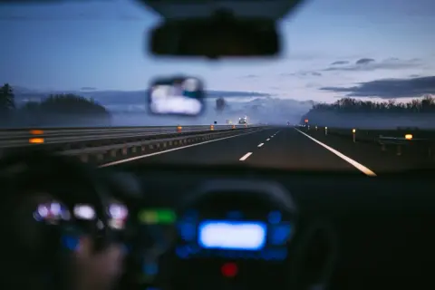 Conduite de nuit sur une autoroute italienne, respectant la limitation de vitesse. Brouillard léger, lumières des phares et du tableau de bord.