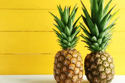 Dwa soczyste ananasy na tle żółtej deski. Poznaj ich bogactwo witamin i minerałów – ananas wartości odżywcze.