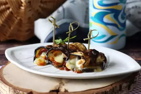 Grillad aubergine rullad med ost och tomatsås, serverad på en vit tallrik. Perfekt för picknick!