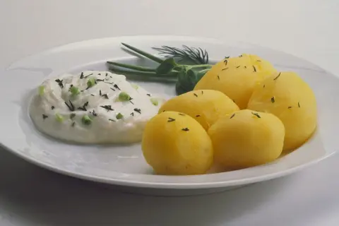 Kartoffeln mit Quark, garniert mit Schnittlauch und Dill, auf einem weißen Teller. Ein einfaches, aber köstliches Gericht.