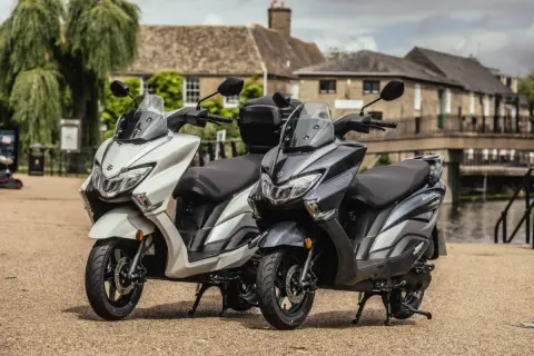 Dwa skutery Suzuki Burgman 125, jeden biały, drugi grafitowy, stoją obok siebie. Sprawdź suzuki burgman 125 cena!