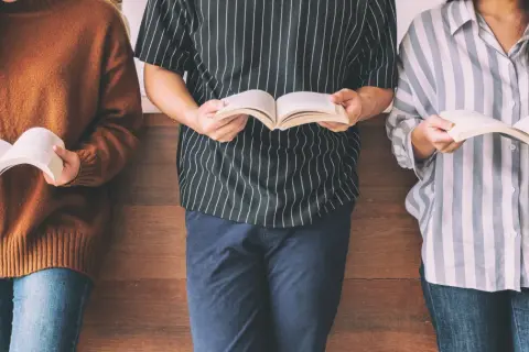 Trzy osoby stojące i czytające książki.