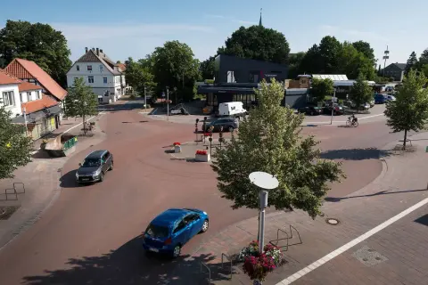 Ein sonniger Tag im **shared space Bohmte**. Autos fahren durch den Kreisverkehr, ein Radfahrer genießt die Fahrt.
