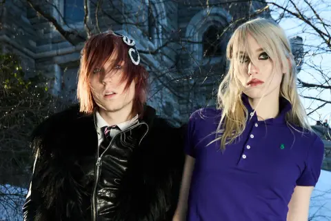 Frost Children setlist: A person with red hair and a black furry jacket stands next to a person with blonde hair in a purple polo shirt.