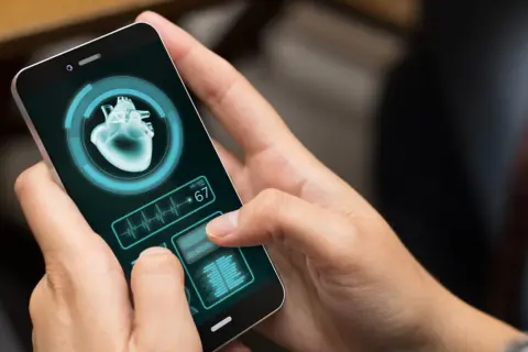 Dłoń trzyma smartfon z aplikacją zdrowie, wyświetlającą obraz serca i tętno 67.