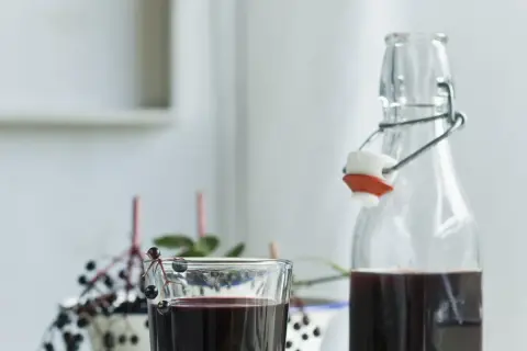 Sok z czarnego bzu przepis babci. Ciemny, zdrowy napój w szklance i butelce, ozdobiony gałązką z owocami.