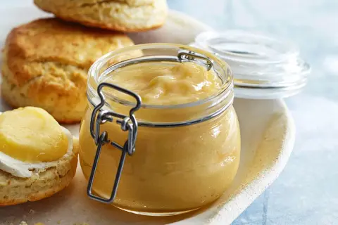 En burk med hemgjord lemon curd står bredvid scones. Perfekt för ditt lemon curd recept!