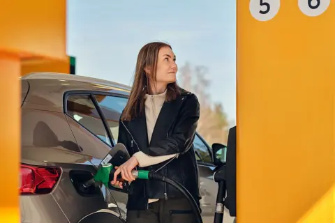 Kvinna tankar sin bil med hvo diesel vid en gul pump.