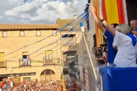 Gente celebra las fiestas de Utebo, ondeando banderas y lanzando confeti desde un balcón.