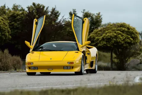 Żółty Lamborghini Diablo z otwartymi drzwiami, zaparkowany na drodze wśród zieleni.