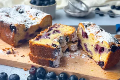 Saftiger skyrkuchen mit heidelbeeren, bestäubt mit Puderzucker. Frische Heidelbeeren liegen daneben.