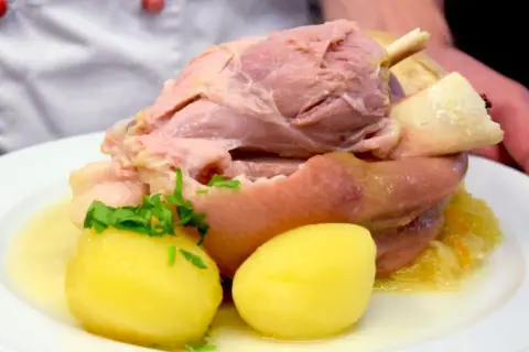 Ein deftiges Eisbein mit Sauerkraut und Kartoffeln, serviert in einem Topf.