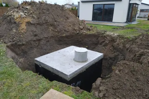 Instalacja odprowadzenia wody z rynien do gruntu. W wykopie widoczny betonowy zbiornik z włazem.