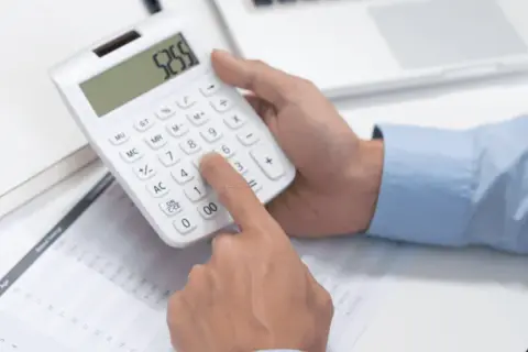 Dłoń naciska klawisze kalkulatora, obliczając wzór na moc prądu. Na stole leżą dokumenty i tablet.