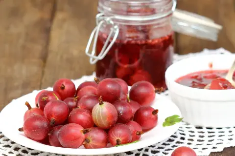 Frische Stachelbeeren auf einem Teller, daneben ein Glas mit Stachelbeermarmelade und eine Schale mit Marmelade. Perfekt, um sie mit Joghurt zu mischen.
