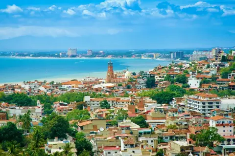 Vista panorámica de una ciudad costera en México, con casas de tejas rojas, una iglesia con cúpula y edificios modernos junto al mar azul. ¡Un sueño para vivir en México!
